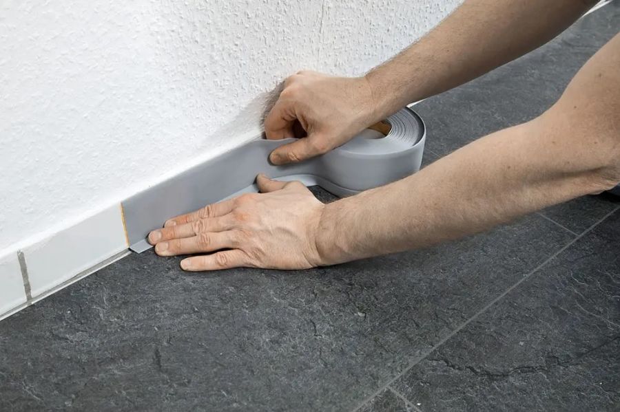 Hände drücken eine selbstklebende Weichsockelleiste an eine Wand, um den Übergang zwischen Boden und Wand sauber abzuschließen.