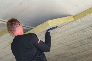 Mann legt Dämmplatte an Kellerwand an