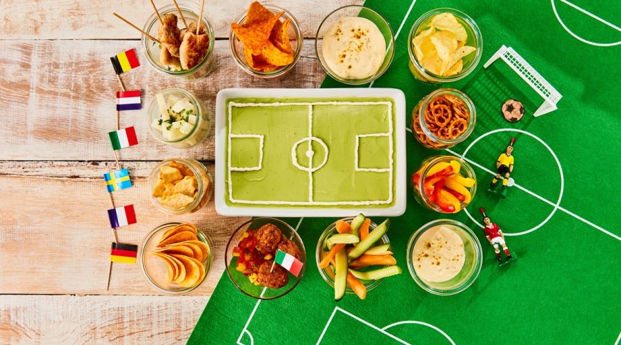 Kuchen in Form eines Fußballstadions, darum sind Snacks gruppiert